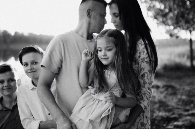 A serene black and white portrait of a family standing by a lake.