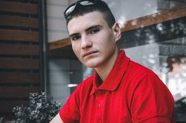 Portrait of a young man wearing a red polo shirt indoors, looking directly at the camera.