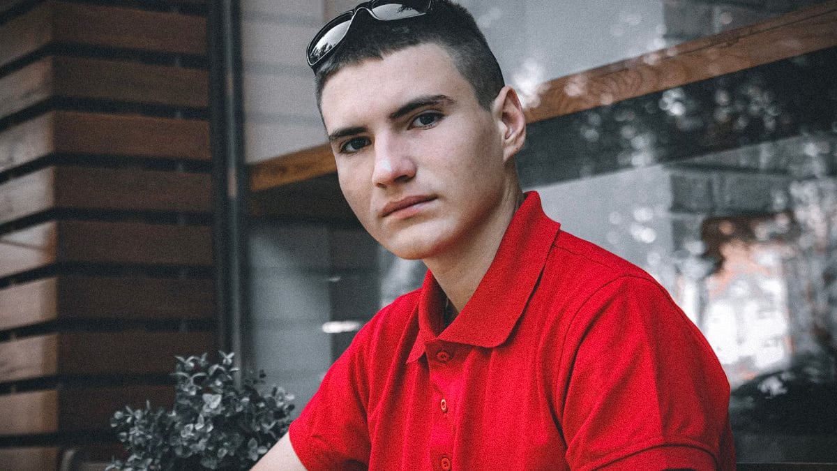 Portrait of a young man wearing a red polo shirt indoors, looking directly at the camera.